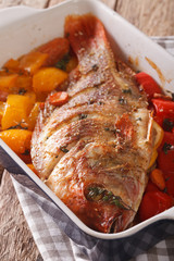 Tilapia fish baked with bell peppers, carrots and thyme close up in baking dish. vertical