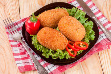 three fried breaded cutlet with lettuce on a black plate and wooden background