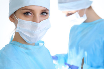 Close up of surgeon woman looking at camera while colleagues performing in background in operation...