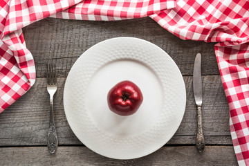 Table set with red apple on white plate with knife and fork with red checkered napkin around .