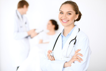 Cheerful smiling female doctor on the background with physician and his patient in the bed. High level and quality of medical service concept.