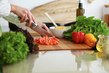 Closeup of human hands cooking vegetables salad in kitchen on the glass table with reflection. Healthy meal and vegetarian concept