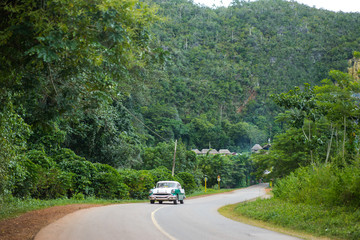 Green retro car is riding on the village road in tropical mountains at summer sunny day