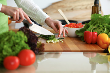Closeup of human hands cooking vegetables salad in kitchen on the glass table with reflection. Healthy meal and vegetarian concept