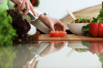 Closeup of human hands cooking vegetables salad in kitchen on the glass table with reflection. Healthy meal and vegetarian concept