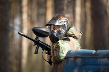 girl playing paintball in overalls with a gun.