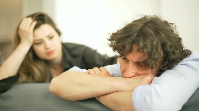 Woman comforting her worried boyfriend while sitting on the sofa
