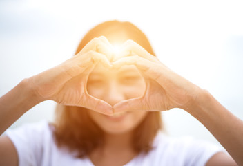 Couple doing heart shape with their hands on lake shore.