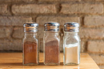 Three bottles of coffee ingredients on wooden bar with grunge brick block wall.
