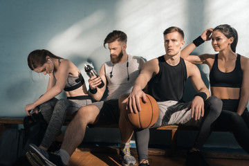 thoughtful sporty men and women sitting on bench in gym