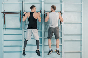 back view of sporty men exercising on sport equipment in gym