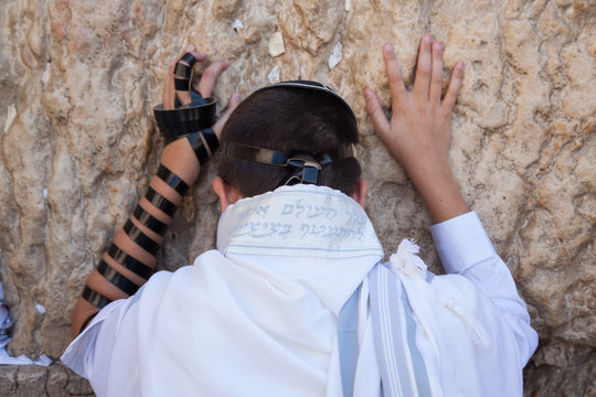jewish teenager celebrate bar mitzvah at the wailing wall and praying with hands on the stones