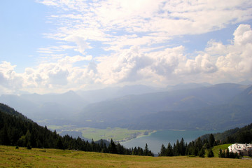 Fototapeta na wymiar Travel to Sankt-Wolfgang, Austria. The view on the green forest and a meadow with a lake and the mountains on the background.