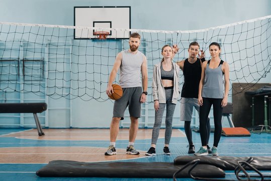 Sporty Young People Standing With Ball And Looking At Camera In Gym