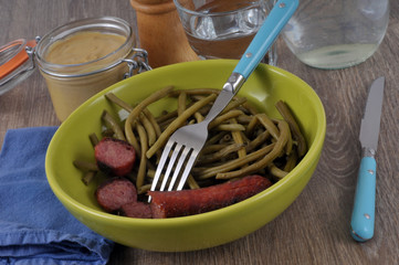 Assiette avec des haricots verts et une saucisse à côté d'un pot de moutarde 