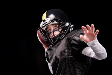 Little boy american football player in uniform throwing ball on black