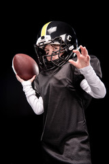 Angry little boy in uniform playing american football on black