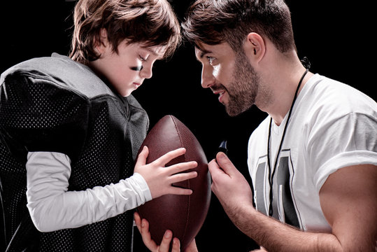 Side View Of Trainer And Boy With Rugby Ball Standing Face To Face On Black