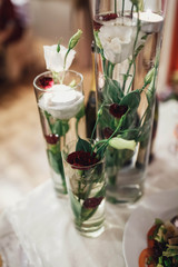 delicate white flowers with green leaves in transparent vases with water
