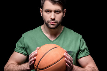 portrait of serious man holding basketball ball in hands on black