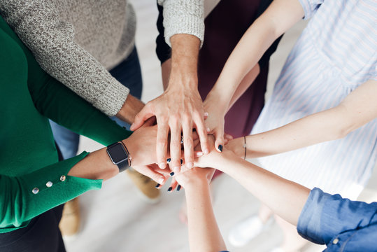 Group of co-workers standing in a circle with their hands in a huddle
