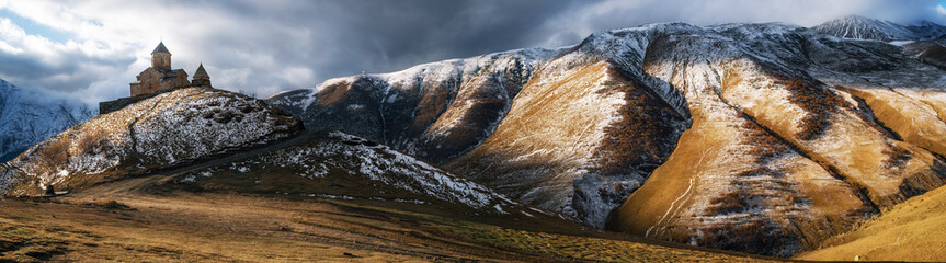 Panoramic view of Caucasus mountains, Gergeti Trinity church Tsminda Sameba against the stormy...