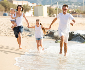 parents with two kids jogging on beach .