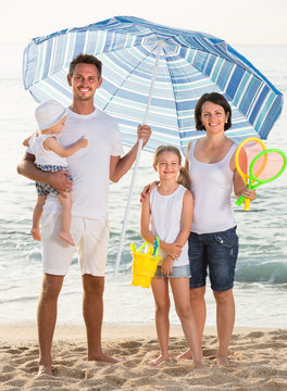 Family Under Sun Umbrella On The Beach