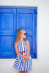 Adorable little girl in front of blue door outdoors at typical greek traditional village on Mykonos in Greece