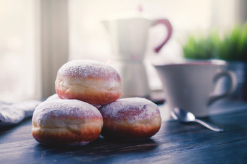 Jelly filled doughnuts on a kitchen table in the morning, coffee mug and pot in the background