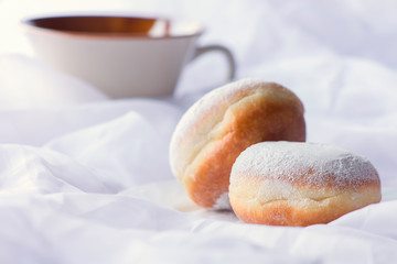 Two jelly filled doughnuts and a coffee mug in white sheets on a bed