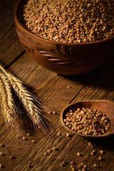  buckwheat in a wooden bowl on a wooden background near the ears of wheat. Wooden spoon with buckwheat
