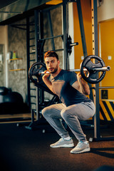 Fototapeta na wymiar Handsome man doing squats with weights in the gym
