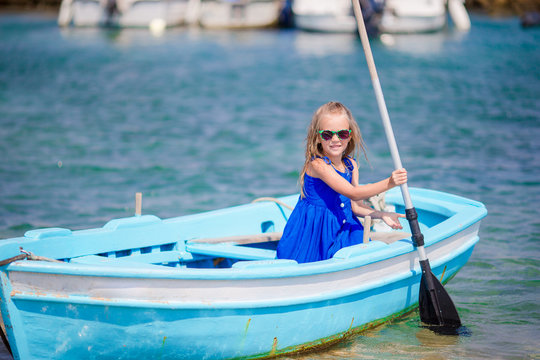 Cute girl in blue boat in the sea bay near the town of Mykonos in Greece. Little kid enjoy swimming in the small boat.