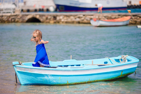Little girl in blue boat in the sea bay near Mykonos in Greece. Little kid enjoy swimming in the small boat.