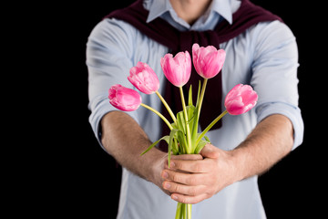 Close-up partial view of man presenting beautiful pink tulips on black, international womens day concept