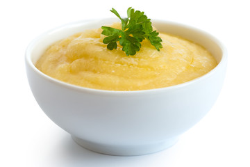 Cooked cornmeal polenta with green parsley in white ceramic bowl isolated on white.