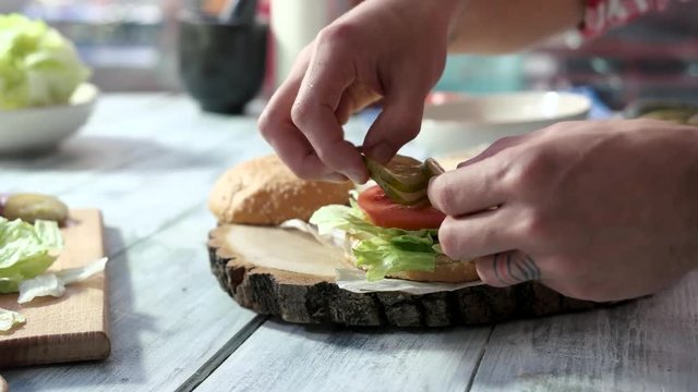 Hands making sandwich with vegetables. Tomato, sliced pickle and onion. Vegetarian burger ideas.