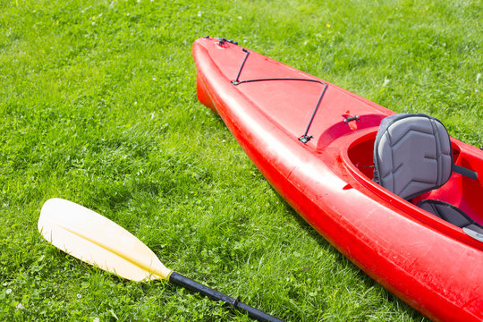 Red kayak and yellow row lays on the green grass and waiting for the journey