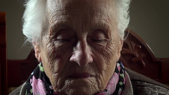 Vold grandmother sitting looking at the camera and closes her eyes