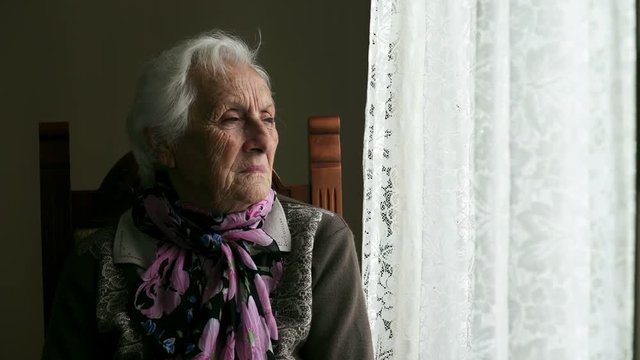  sad and pensive old woman sitting near the window