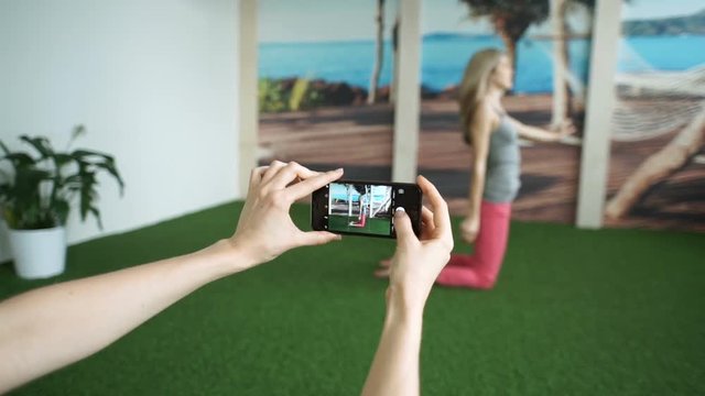 Beautiful woman taking photo with smartphone for social media. Close up of female hands taking photo of her friend in fitness hall. Concept for yoga sport and healthy lifestyle.