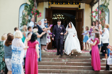 Guests are greeted wedding couple with petals of roses at exit from church.