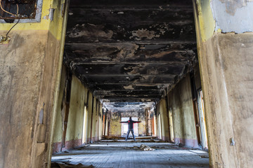 Fototapeta na wymiar Long corridor of abandoned and burnt building with a man who stands in the center and spreads his hands