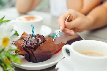Chocolate muffin with one candle, cups with coffee on wooden table .