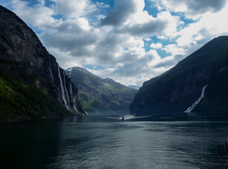 Small boat travelling on river between giant mountains