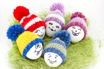 Fototapeta na wymiar Easter eggs on green sisal. Emoticons in knitted hat with pom-poms. Handmade.