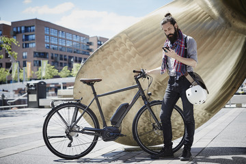 Man with electric bicycle looking at his cell phone