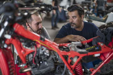 Fototapeta na wymiar Two mechanics working on motorcycle in workshop together