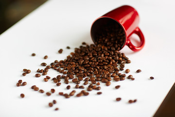 Background image: Seeds of rich freshly roasted coffee spilling out of tipped red cup to white table